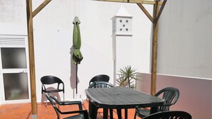 En uteplats med ett bord och stolar, ett grönt parasoll och en krukväxt.