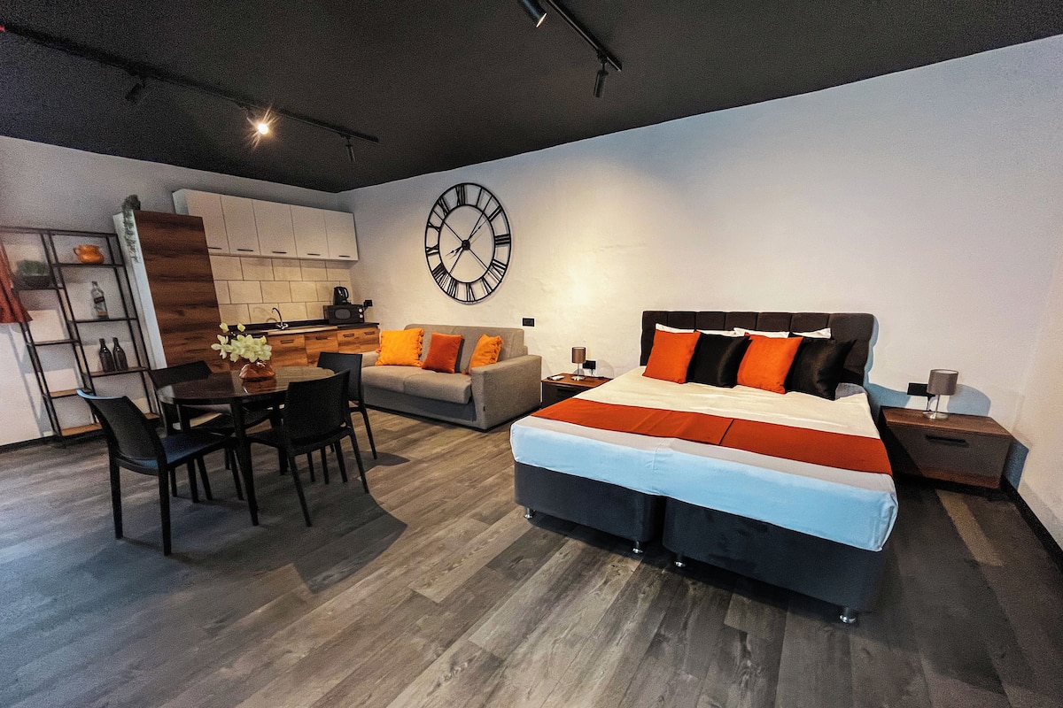 Un dormitorio moderno con una cama grande, una zona de comedor y una cocina al fondo.