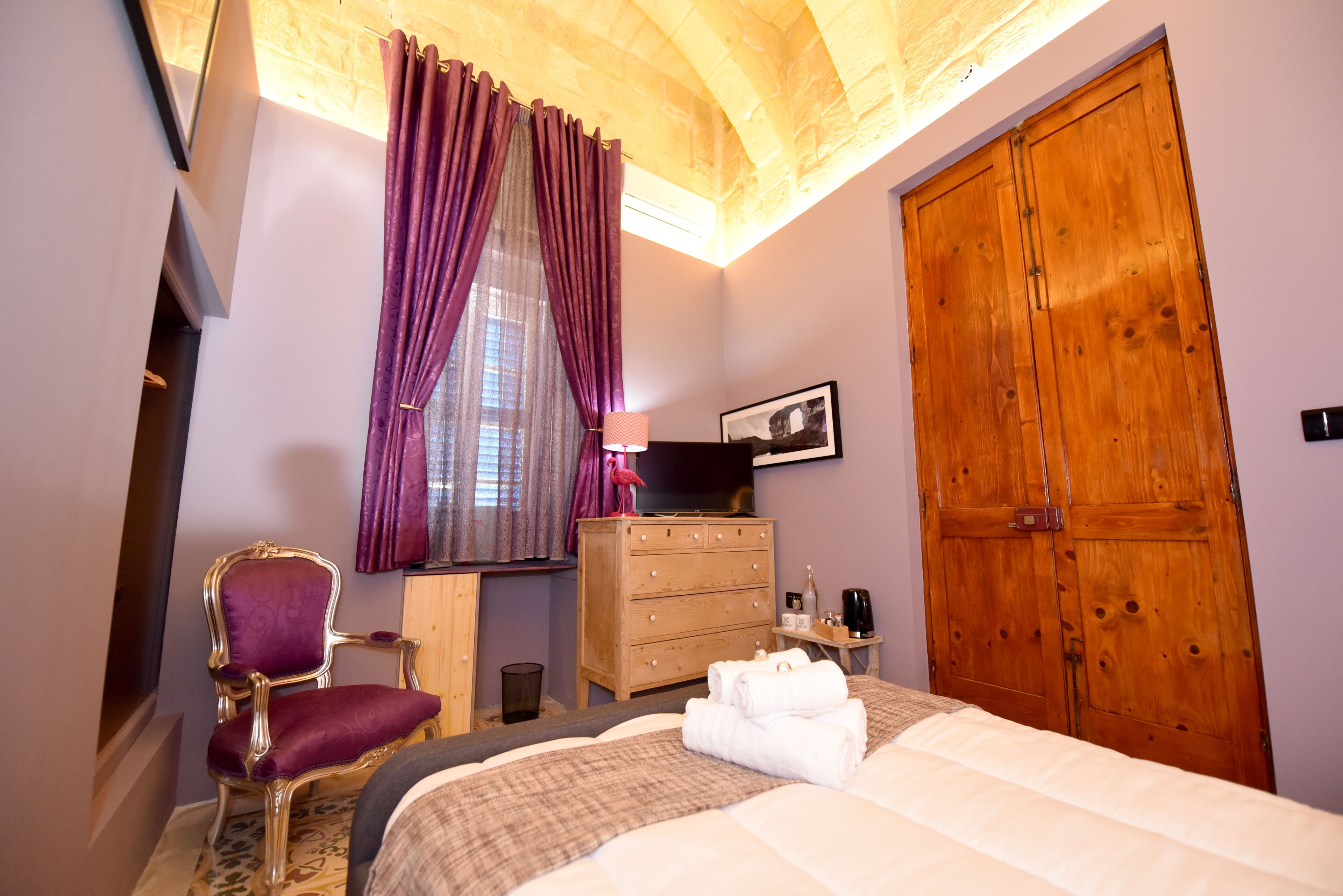 Une chambre à coucher comprenant un lit, une armoire en bois, une chaise, une commode et une fenêtre avec des rideaux.