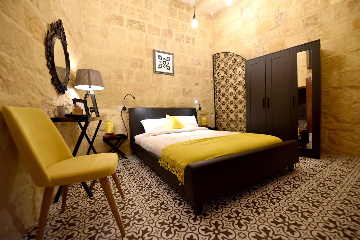 Un dormitorio con cama, una silla, armario, espejo y lámpara.