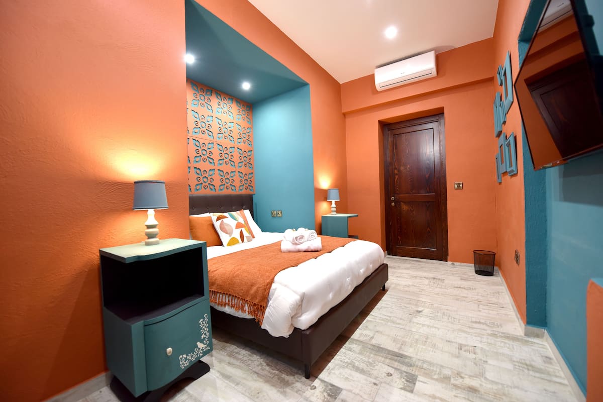 Un dormitorio con cama, mesitas de noche, un papel tapiz decorado y una puerta.