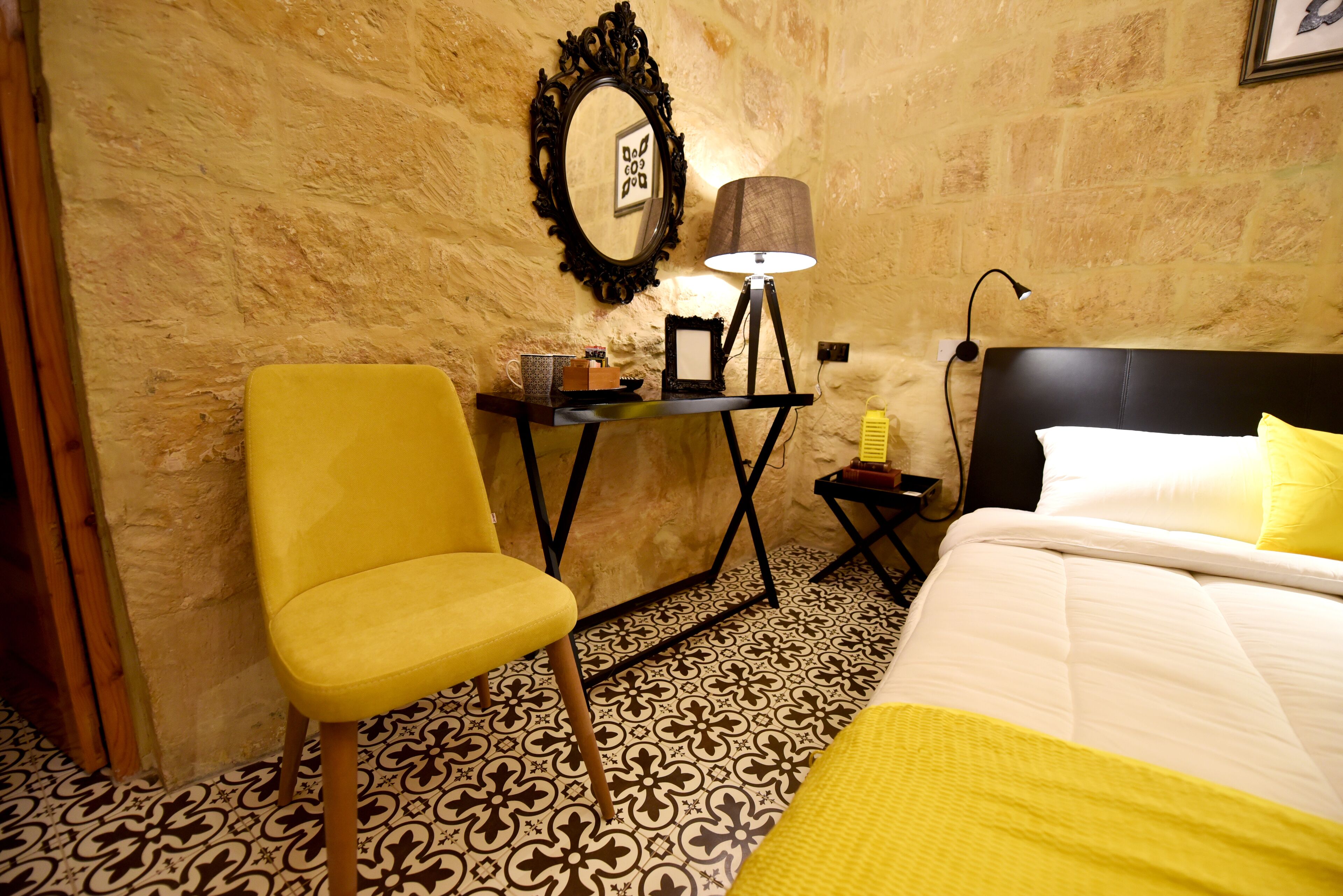 Une chambre d’hôtel avec un lit, un bureau doté d’une lampe, une chaise et un sol à motifs.