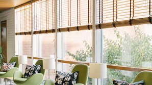 A modern waiting area with green chairs, patterned cushions, and large windows with blinds.