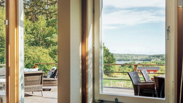 A view from a window overlooking a deck with wicker furniture and a scenic landscape.