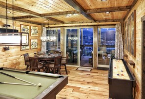 Une pièce au plancher de bois, équipée d’une table de billard, d’un baby-foot et d’un coin repas avec des chaises et une table.