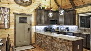 Una cocina con una isla de piedra, armarios oscuros y techo de madera.