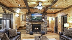 A log cabin interior with a stone fireplace, leather sofas, and a television mounted above it.