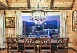 Une salle à manger en bois, dotée d’une grande fenêtre, de chaises en bois et d’un lustre.