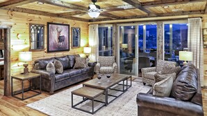 Interior acogedor de una cabaña de madera con techo de madera, sofás de cuero, sillones estampados y un ventanal con vistas al exterior.
