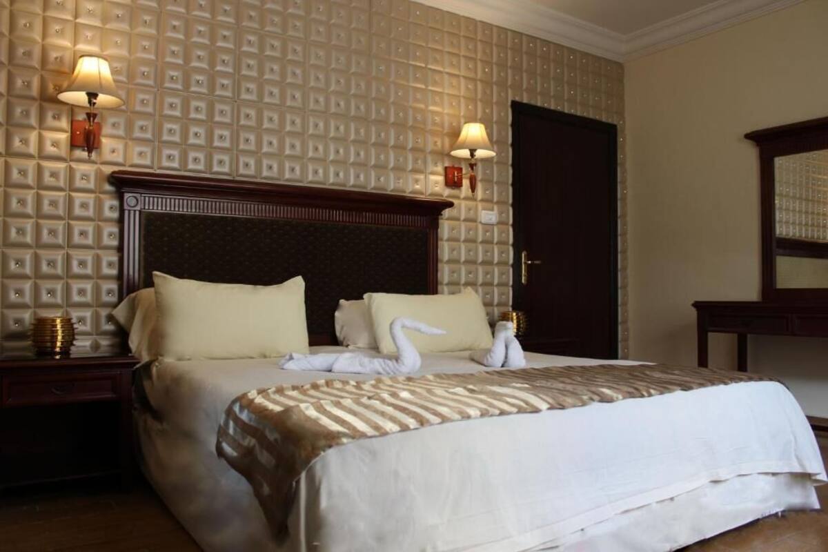 A hotel room with a large bed, two bedside lamps, a wooden headboard, and a patterned wallpaper.
