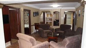 A living room with four armchairs, a coffee table, and a TV. There is a door leading to another room, and a mirror on the wall. - Rana Palace (Amman)