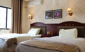 Camera d'albergo con due letti, un'ampia finestra con tende, lampade a parete e quadri incorniciati.