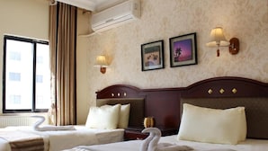 A hotel room with two beds, a large window, and a wall-mounted air conditioner. - Rana Palace (Amman)