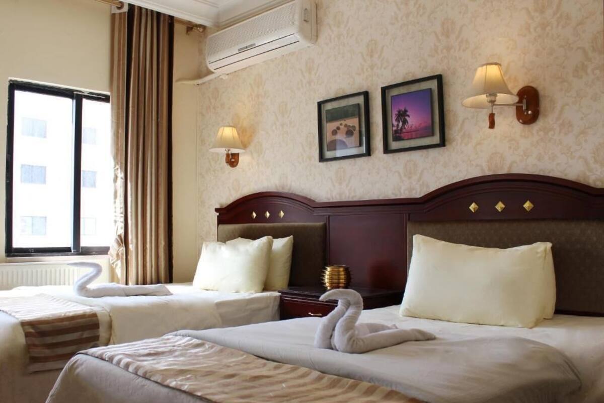 A hotel room with two beds, a large window, and a wall-mounted air conditioner.