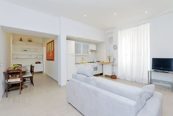 Um apartamento moderno com sala de jantar, cozinha compacta, sala de estar e televisão.
