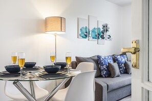 Un coin repas moderne avec une table en verre, des chaises blanches et une lampe. On peut voir trois bols et des verres contenant une boisson jaune sur la table.