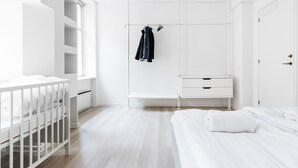 A modern, white-themed bedroom with a crib, a bed, a wardrobe, and a clothing rack. - 120m2 Apartment in Nyhavn (Copenhagen)