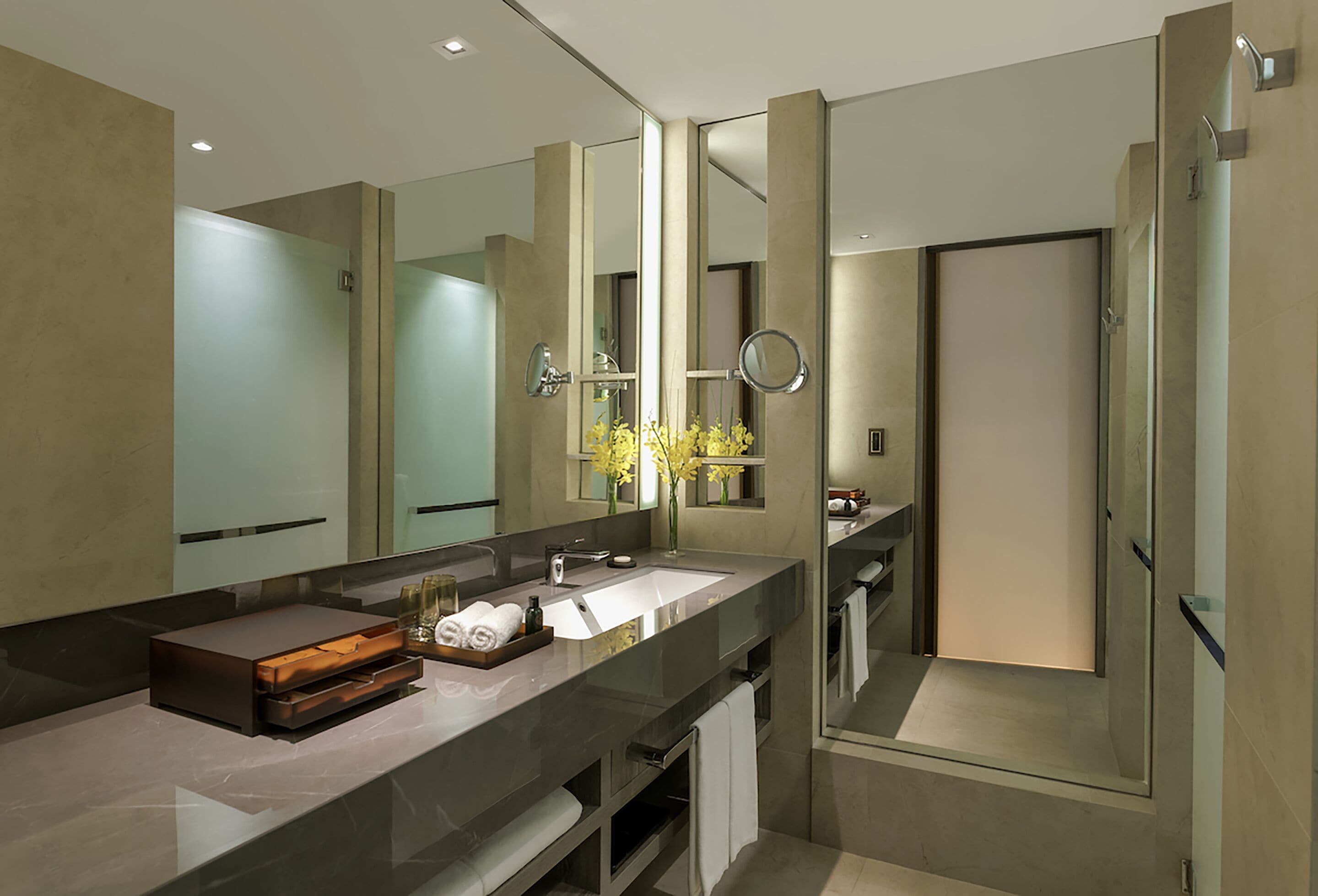 A modern bathroom with a large mirror, a glass shower enclosure, and a marble countertop.