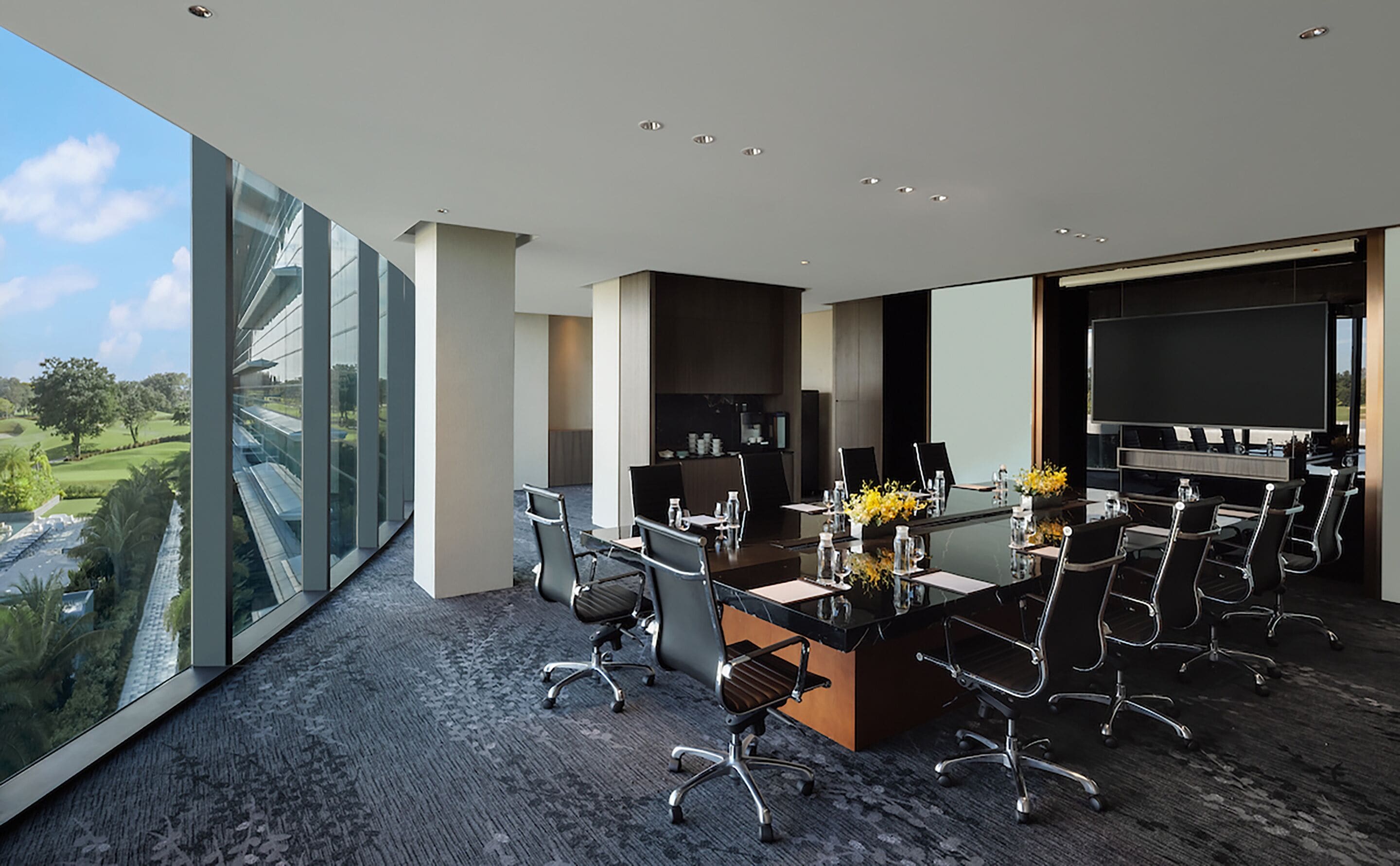 A modern conference room with a large glass wall, a large screen, and a view of a golf course.