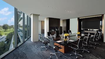 A modern conference room with a large glass wall, a large screen, and a view of a golf course.
