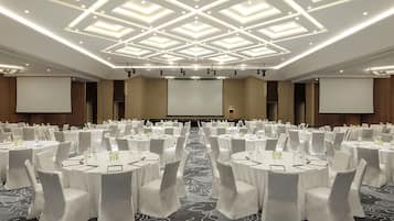 Un salón de conferencias con varias mesas redondas, cada una con mantel blanco y sillas, equipado con tarjetas de identificación y vasos de agua.