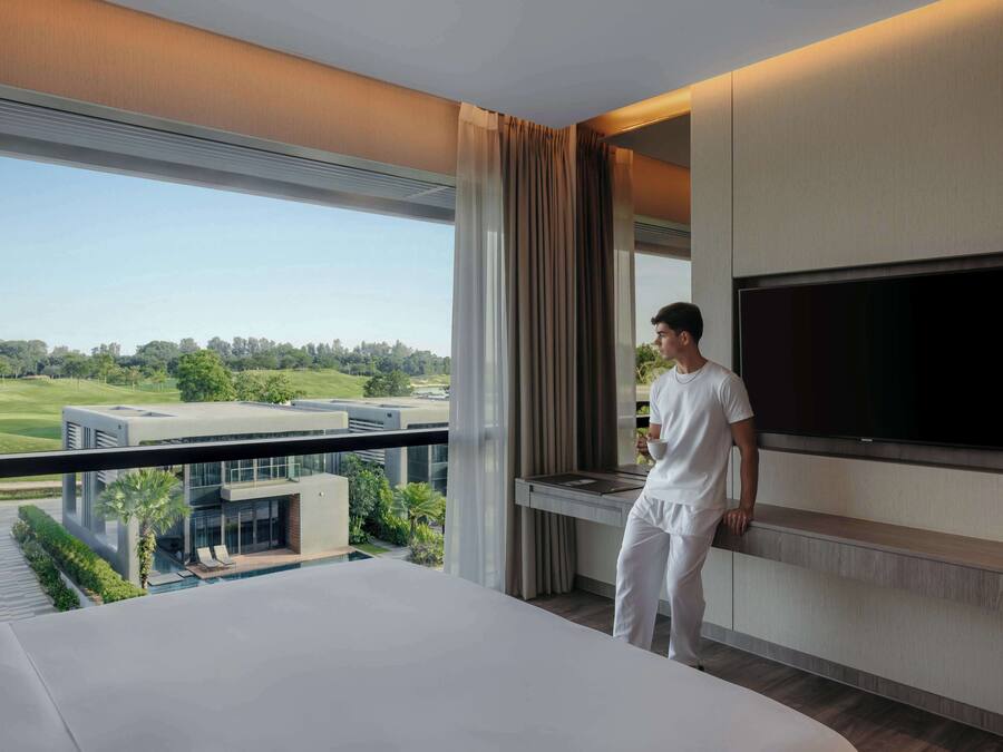 Una camera d'albergo moderna con un letto grande, una TV a schermo piatto montata a parete e un balcone con vista su un campo da golf.