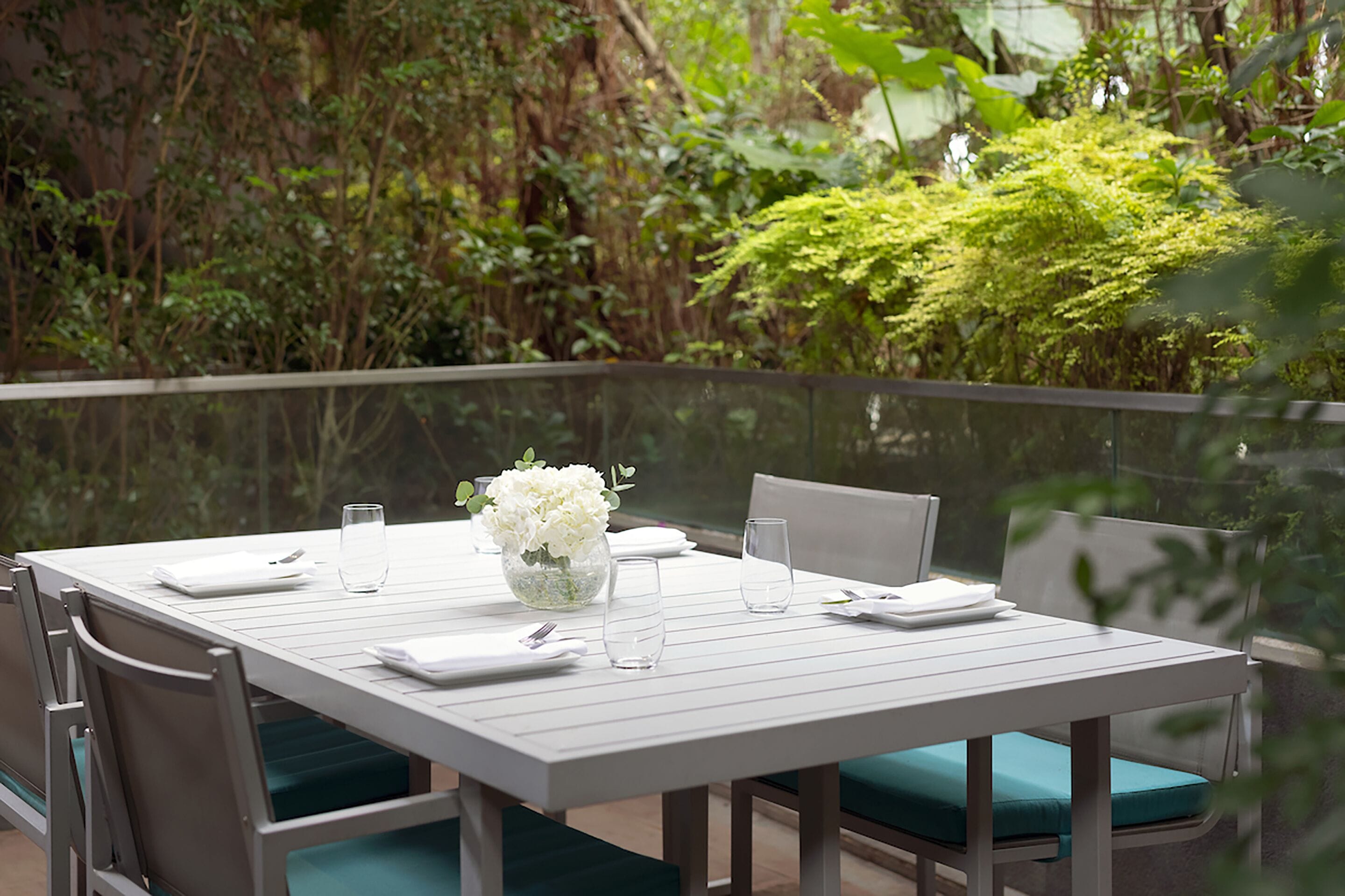 A dining table set with white tableware, a vase of white flowers, and green cushioned chairs.