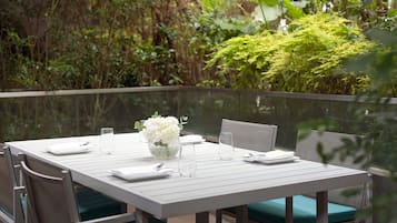 A dining table set with white tableware, a vase of white flowers, and green cushioned chairs.