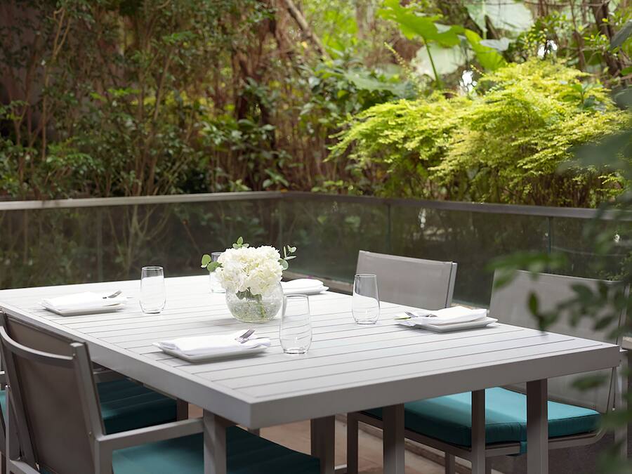 A dining table set with white tableware, a vase of white flowers, and green cushioned chairs.