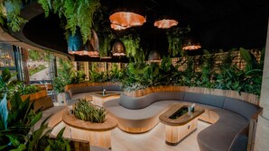 A modern lounge area with a curved sofa, wooden coffee tables, and hanging planters. - Dusit Thani Laguna Singapore (Singapore)