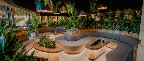 A modern lounge area with a curved sofa, wooden coffee tables, and hanging planters.