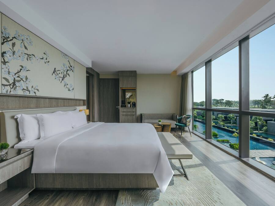 A modern hotel room with a large bed, a view of a swimming pool, and a balcony.