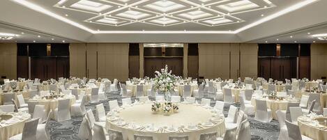 A large banquet hall with round tables, white chairs, and a central floral arrangement.
