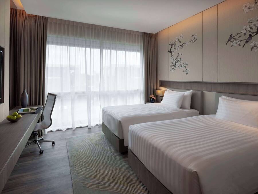 Une chambre d’hôtel avec deux lits, un bureau avec une chaise, une télévision et une grande fenêtre avec des rideaux.