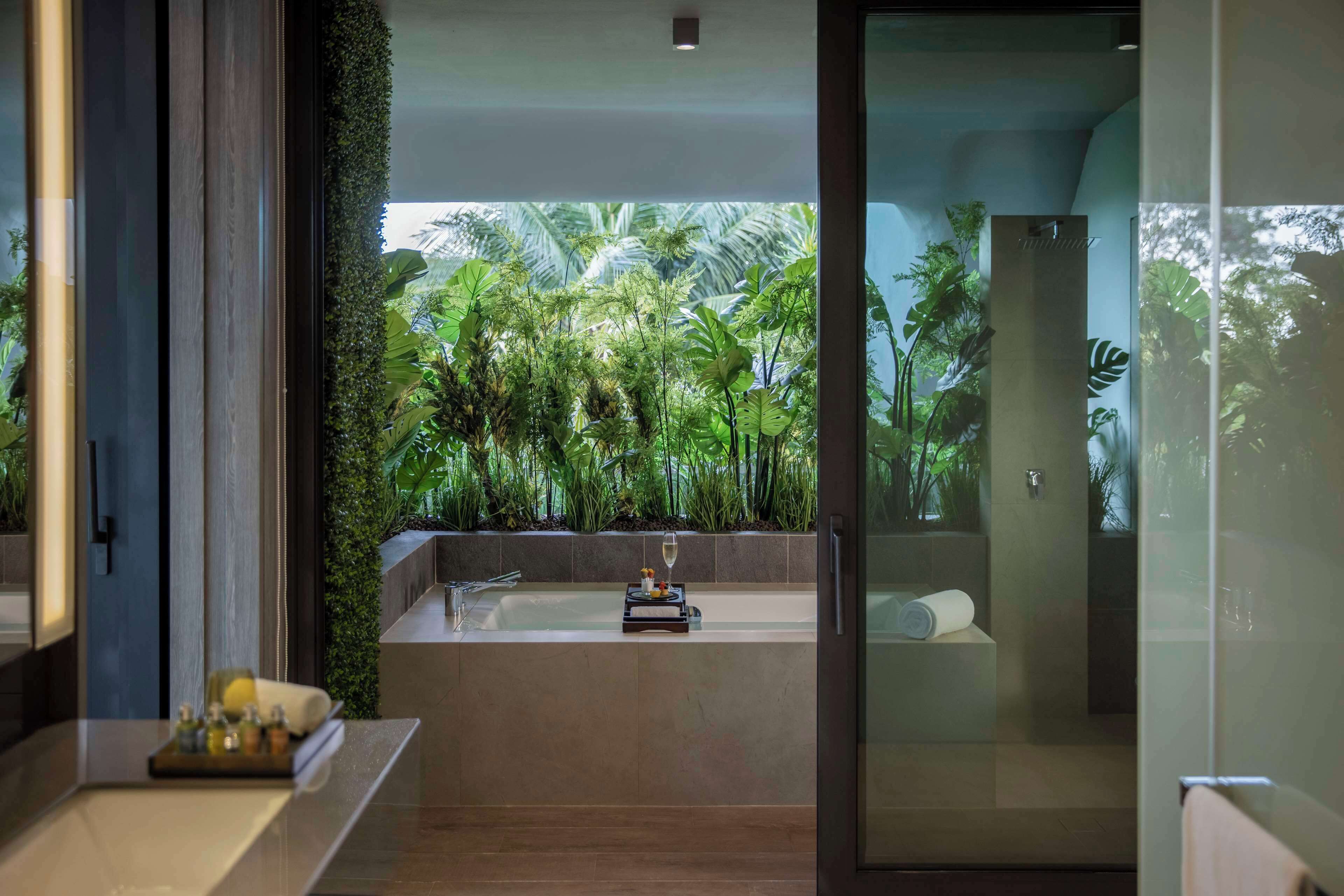 Un baño moderno con una bañera grande, cabina de ducha de vidrio y vistas a exuberante vegetación tropical.