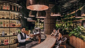 A bar area with a curved wooden counter, shelves with bottles, and hanging pendant lights. - Dusit Thani Laguna Singapore (Singapore)