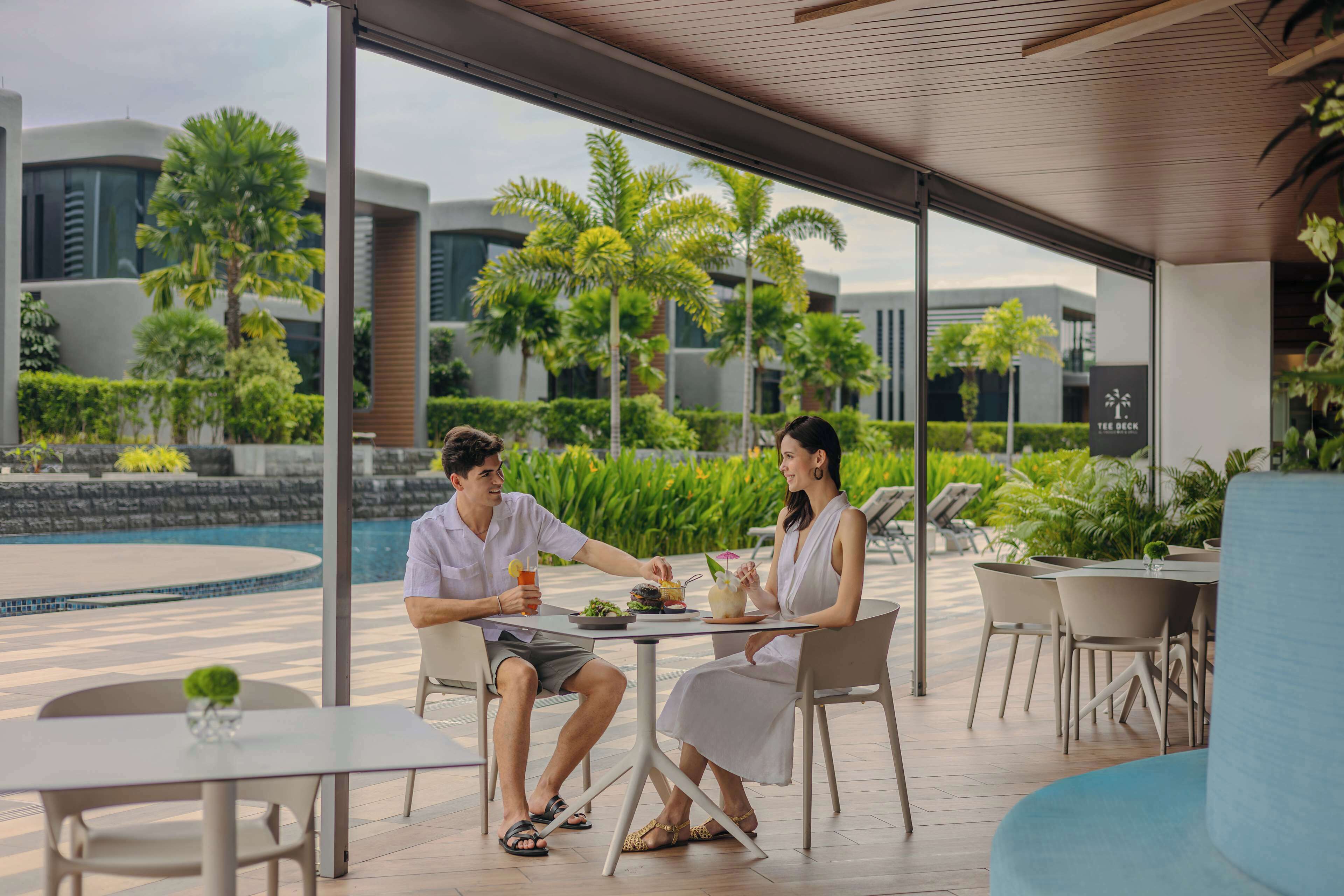 Una pareja cenando en una mesa al aire libre con vista a un edificio moderno y palmeras.