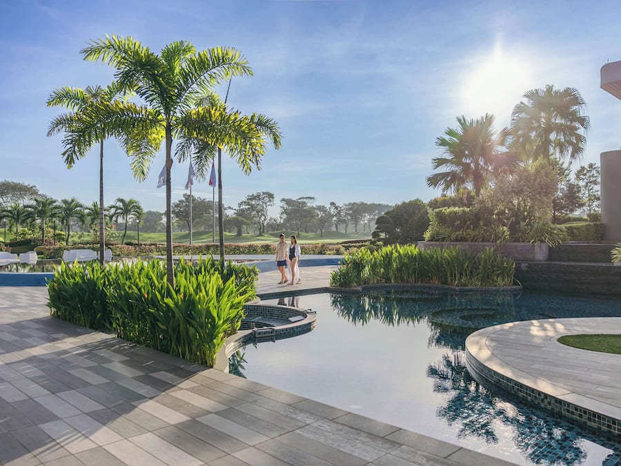 A pool area with palm trees, a tiled deck, and a clear sky.