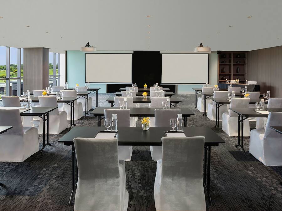 A conference room with tables and chairs, a large screen, and a view of the outdoors.