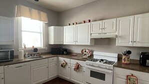 Una cocina con armarios blancos, estufa, pileta y ventana con cortina.