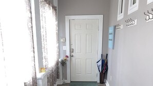 Un pasillo con piso de madera, una puerta blanca y un ventanal con cortinas.