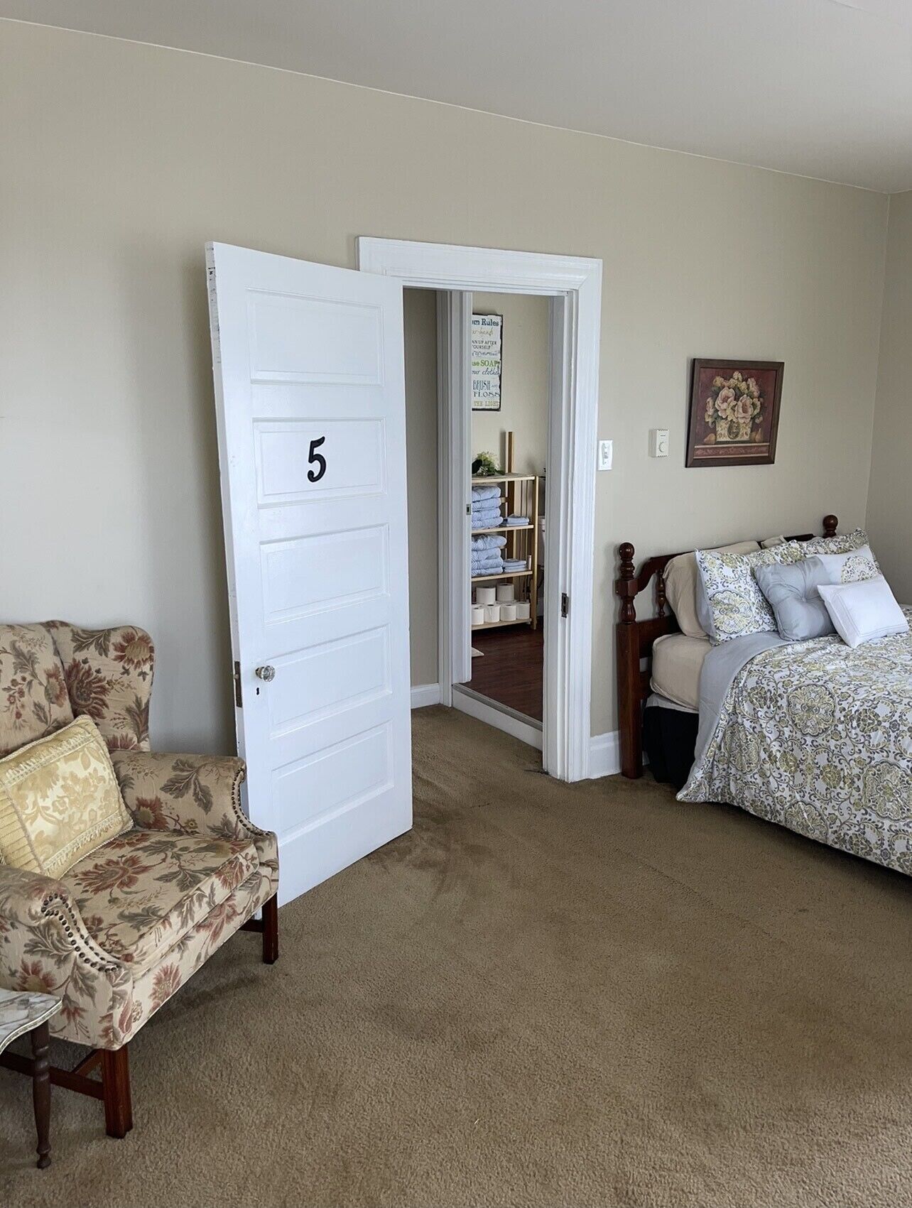 A bedroom with a floral-patterned sofa, a bed with patterned bedding, and a door labeled with the number 5.