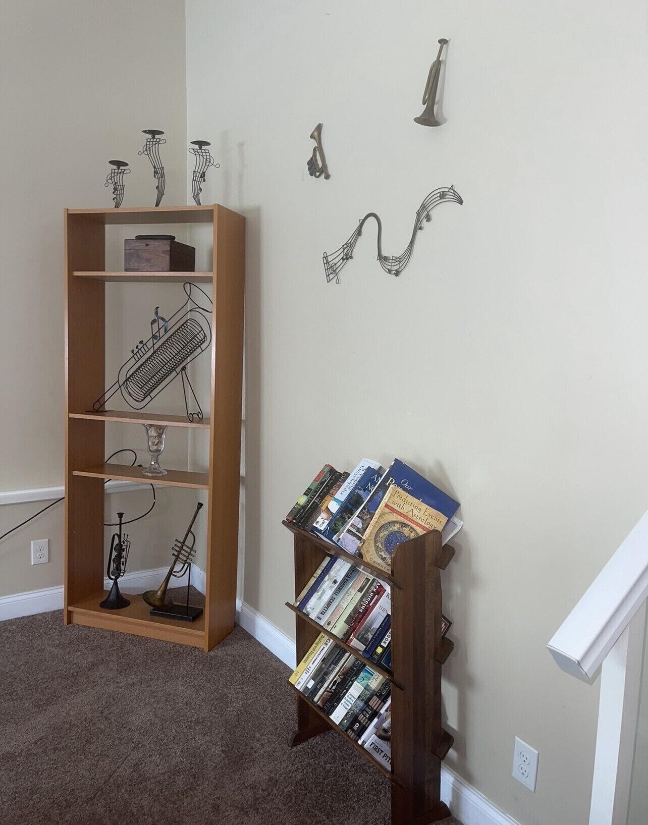 A room with a wooden bookshelf containing books and decorative items, a small table with a glass, and a wall with musical instruments and a book titled "Our Predictions for the Future with Astrology".