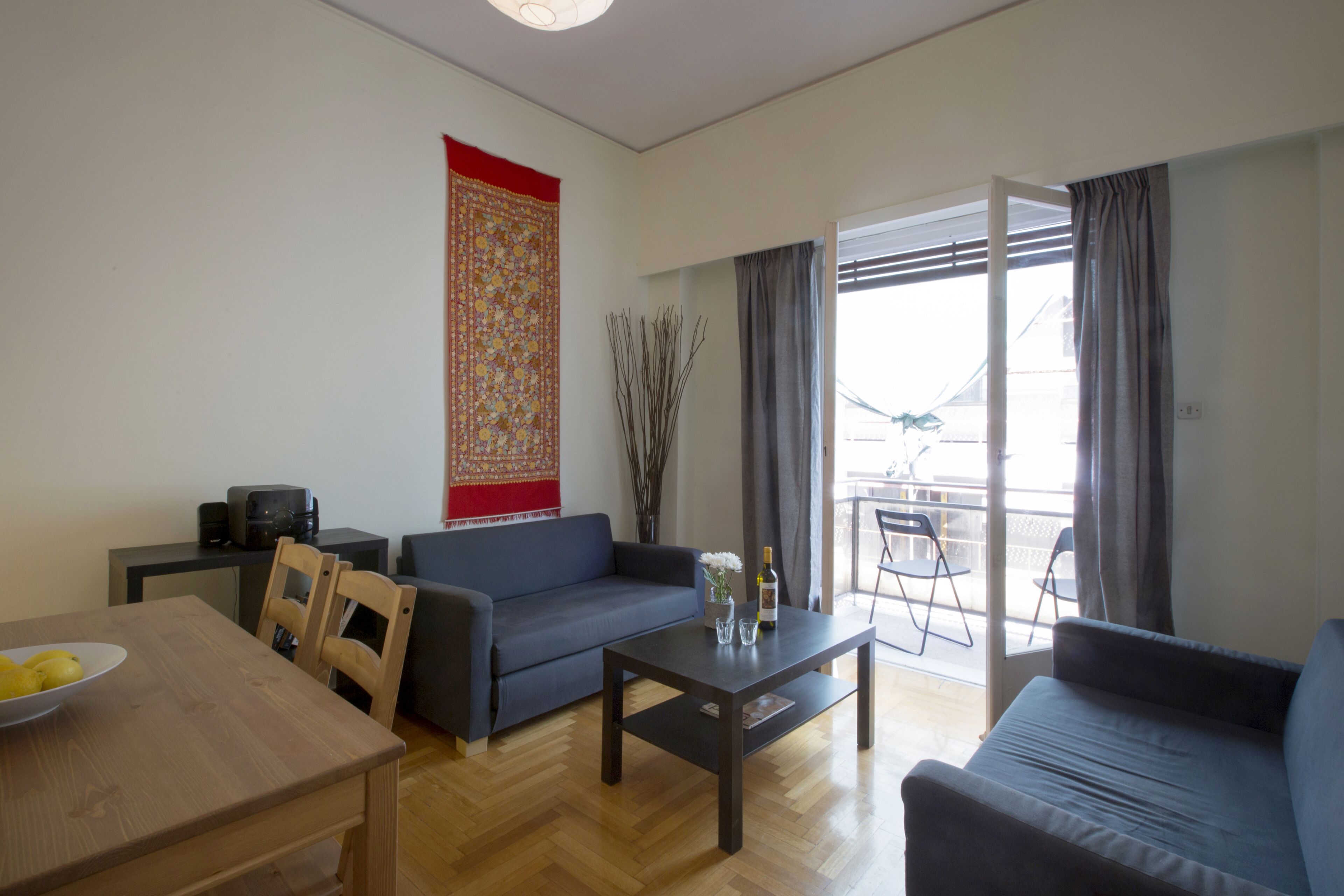 A modern living room with a sofa, a coffee table, and a dining table. There is a balcony with a view.