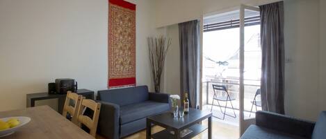 A modern living room with a sofa, a coffee table, and a dining table. There is a balcony with a view.