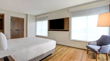 Habitación de hotel con cama, una silla, un televisor en la pared y un ventanal.