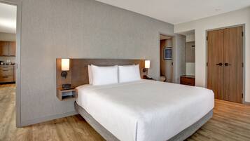 A modern hotel room with a large bed, a bedside table with a lamp, and a wooden wardrobe.