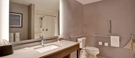 A modern bathroom with a large mirror, two sinks, a toilet, and a shower.