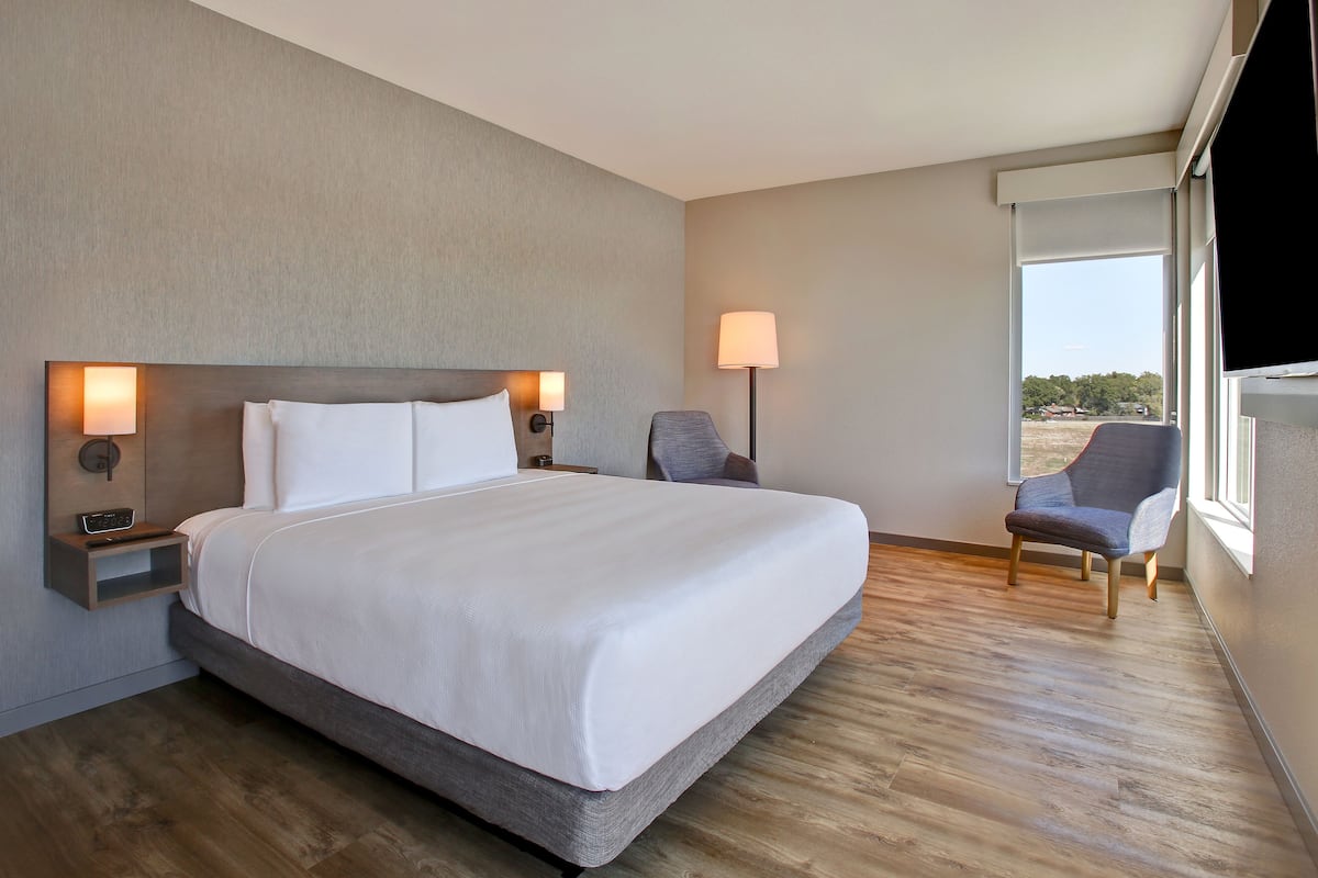 A hotel room with a large bed, bedside tables with lamps, a chair, and a view through the window.
