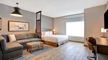 Una habitación de hotel moderna con cama, sofá, escritorio y un ventanal grande.